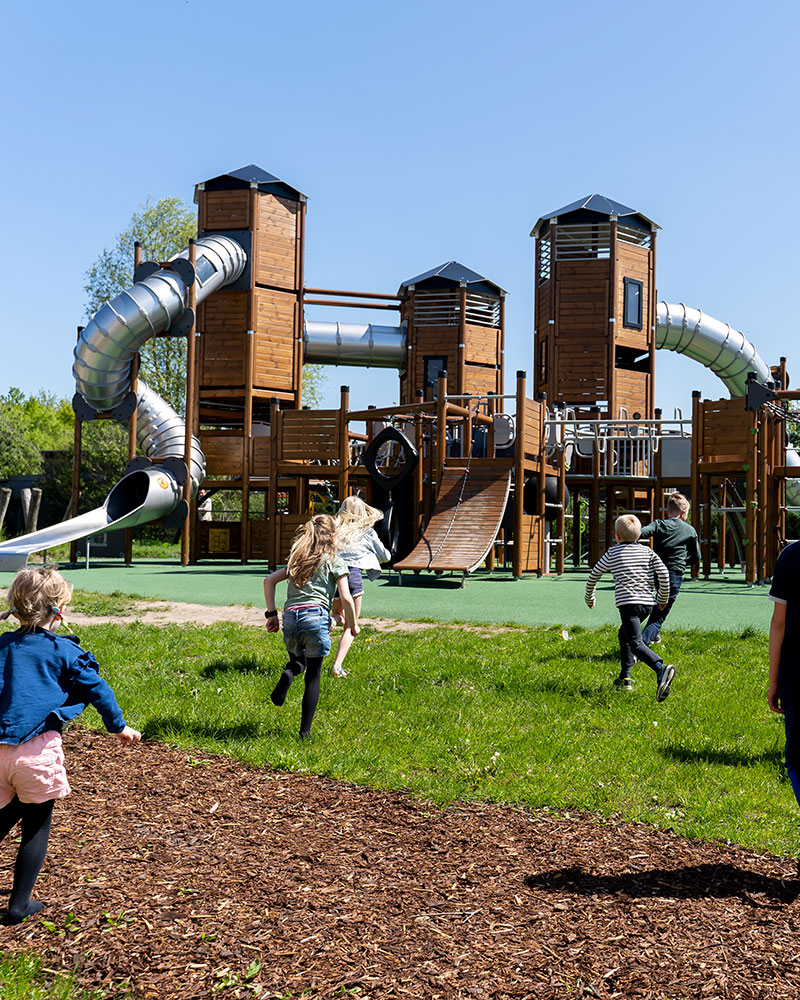 Children run towards a large wooden playground unit.
